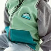 Zoom du manteau à capuchon vert, turquoise et gris en coquille souple, enfant