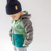 Photo d'un enfant portant le manteau à capuchon vert, turquoise et gris en coquille souple, bébé