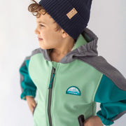 Photo d'un enfant portant le manteau à capuchon vert, turquoise et gris en coquille souple, enfant