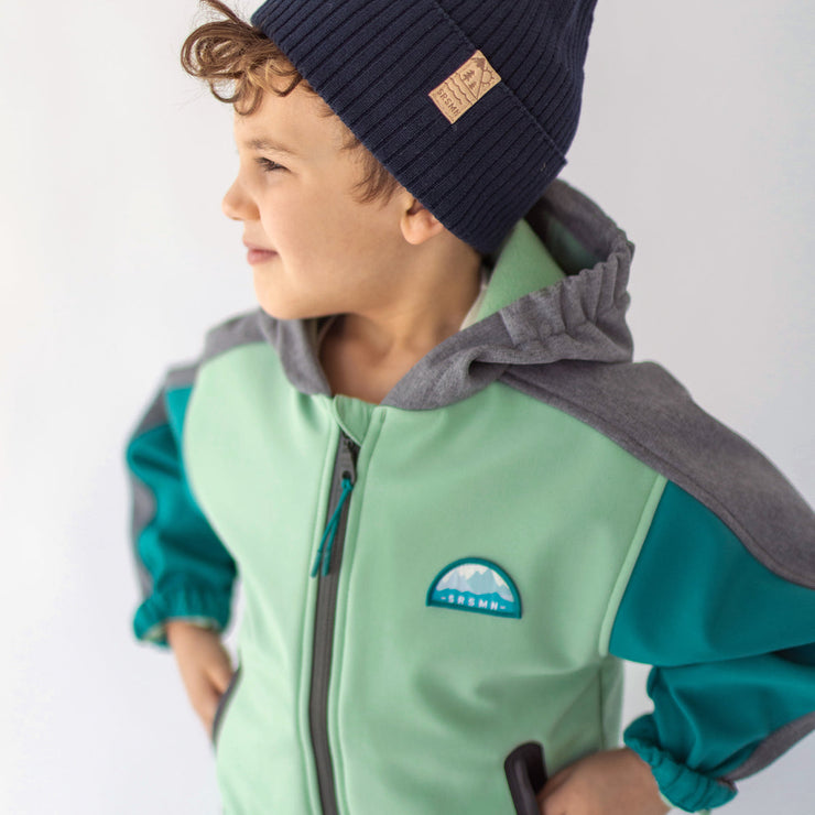 Photo d'un enfant portant le manteau à capuchon vert, turquoise et gris en coquille souple, enfant